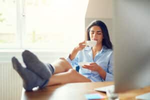 Woman at a desk drinking tea with legs elevated to prevent varicose veins in Portland, OR